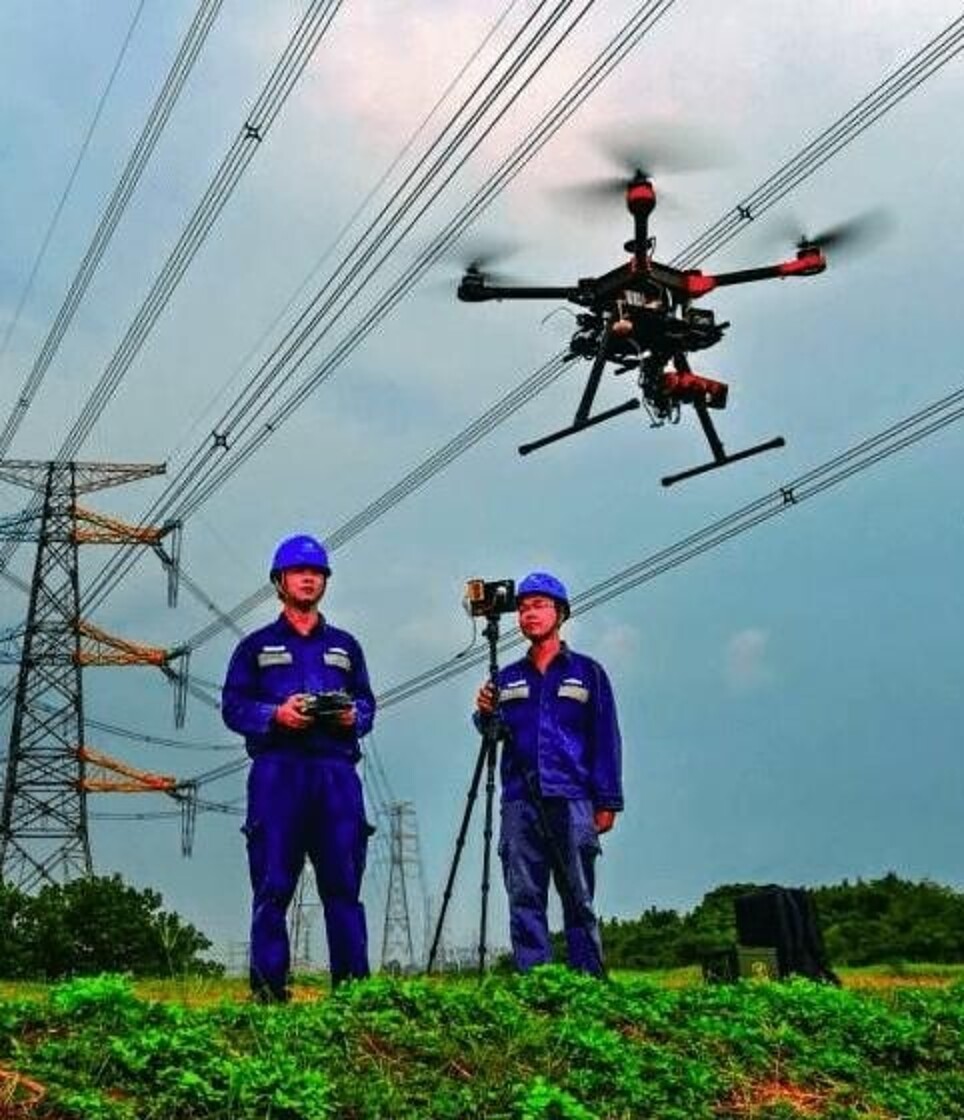 Equipe técnica com capacete fazendo levantamento com drone junto a linhas de transmissão